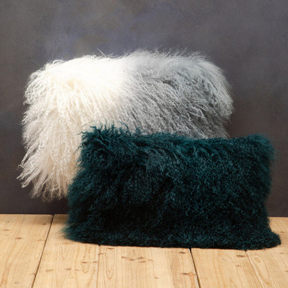 Two fluffy pillows, one white and one green, on a wooden floor against a dark wall.