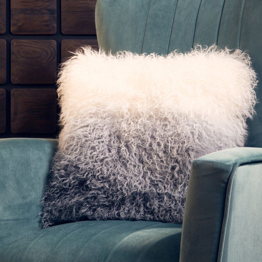 Textured pillow on a teal sofa against a dark brick wall