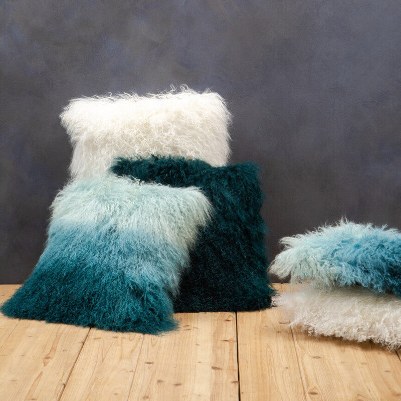 Set of fluffy pillows in white, teal, and blue on a wooden surface with a dark textured wall background.