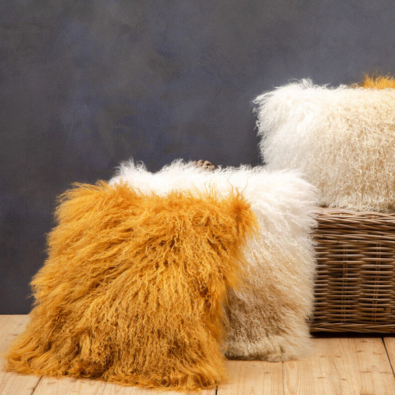 Three fluffy pillows in white, beige, and orange on a wooden surface with a dark textured background.