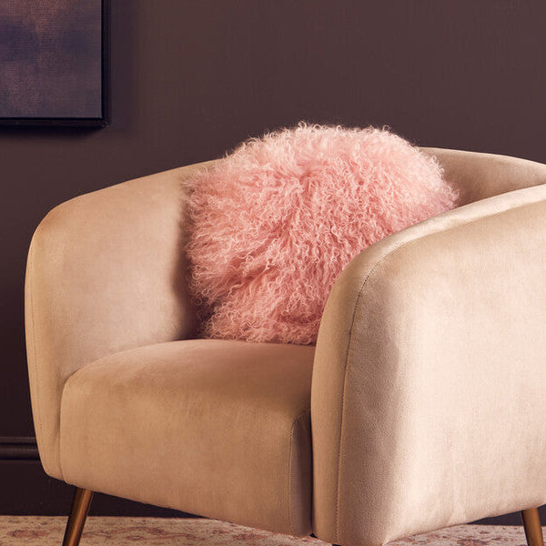 Beige armchair with a pink fluffy pillow against a dark wall.