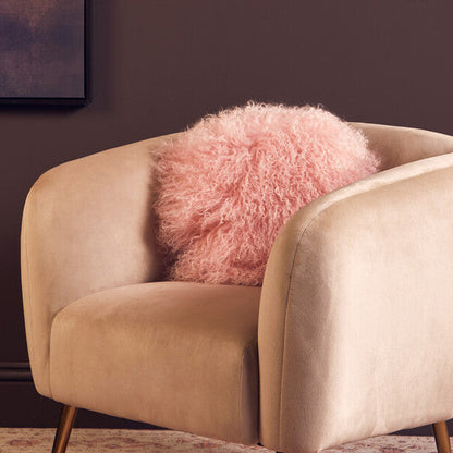 Beige armchair with a pink fluffy pillow against a dark wall.