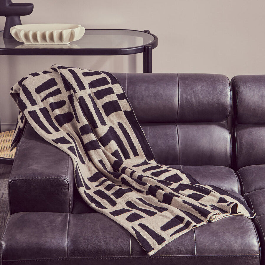 Patterned blanket draped over a dark leather sofa in a living room setting.
