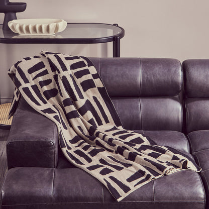 Patterned blanket draped over a dark leather sofa in a living room setting.