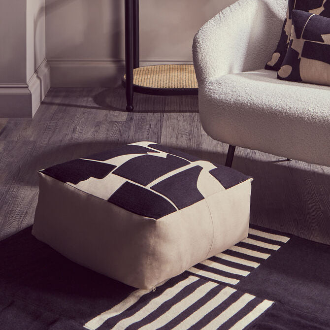 Modern living room with a gray sofa, abstract-patterned cushions, and a geometric rug.