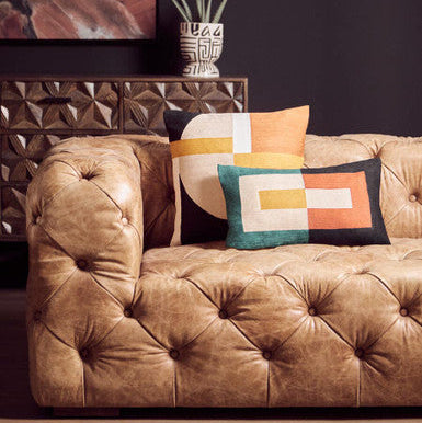Brown tufted sofa with colorful pillows against a dark wall.