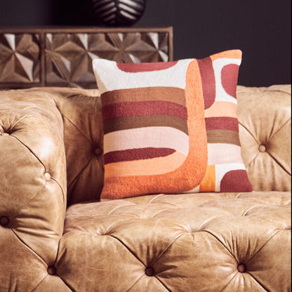 Brown tufted sofa with a colorful pillow against a dark wall.