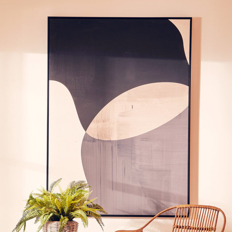 Wicker chair and side tables with a plant against a wall with abstract art