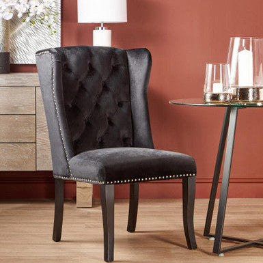 Gray upholstered chair with tufted backrest in a room with a lamp and decorative items.