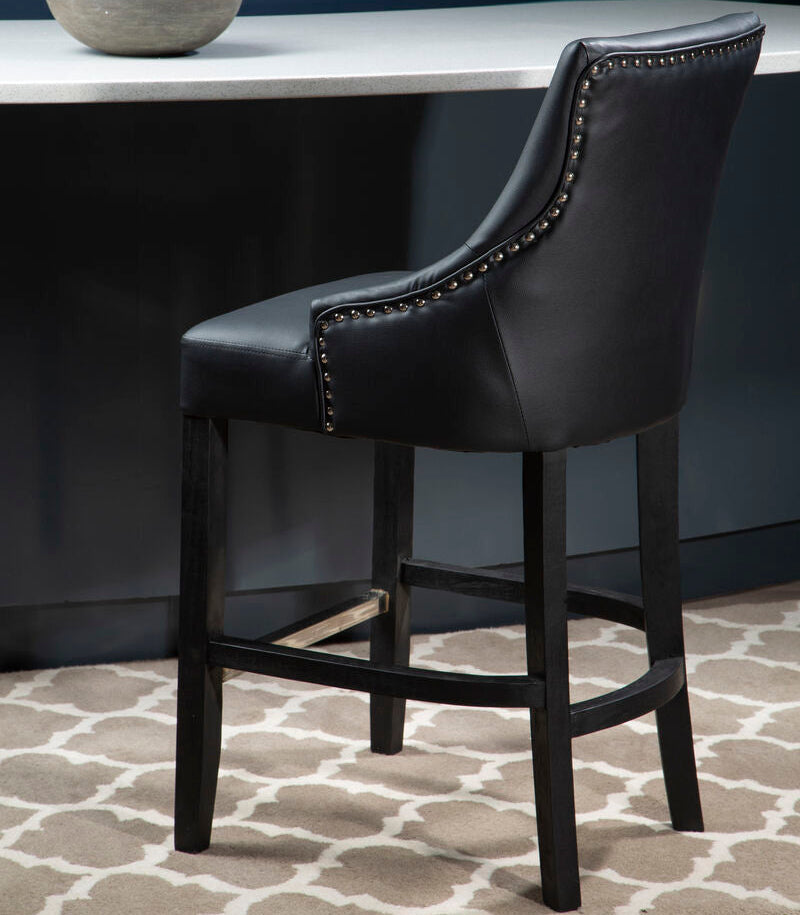 Black leather bar stool with nailhead trim in a room with a dark wall and patterned rug.