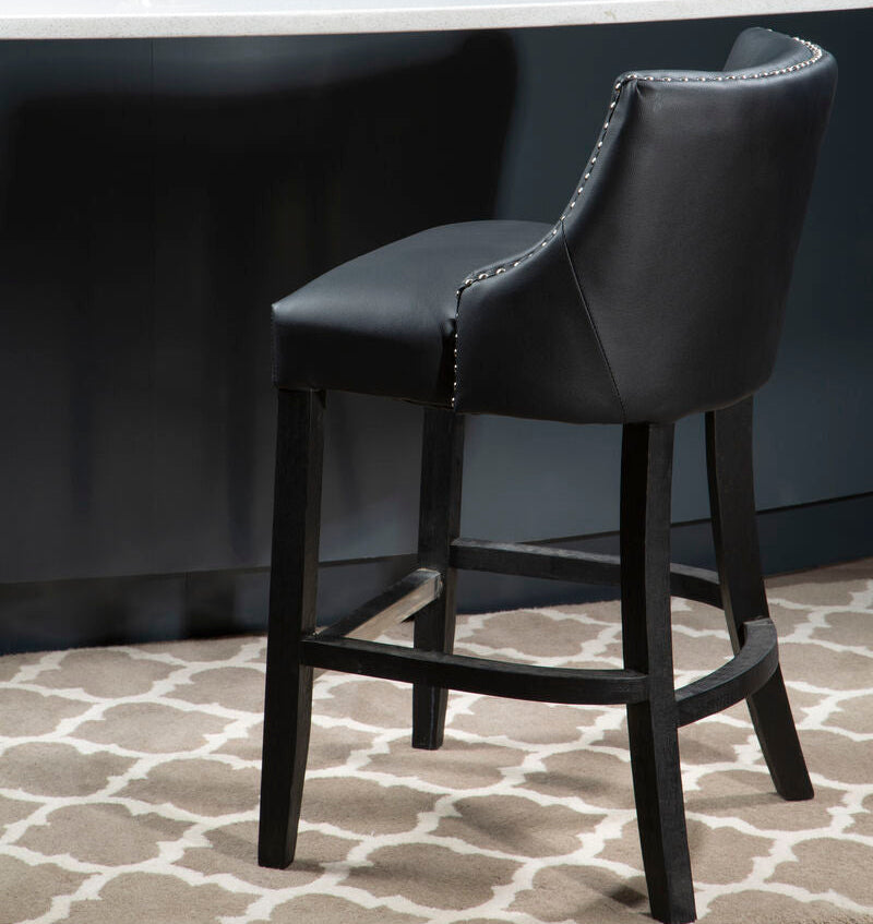 Black bar stool in front of a white counter with a plant on it, against a dark blue wall.