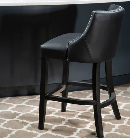 Black bar stool in front of a white counter with a plant on it, against a dark blue wall.