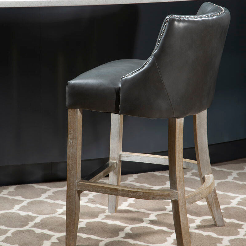 Gray bar stool with wooden legs in front of a white countertop with a plant on it.