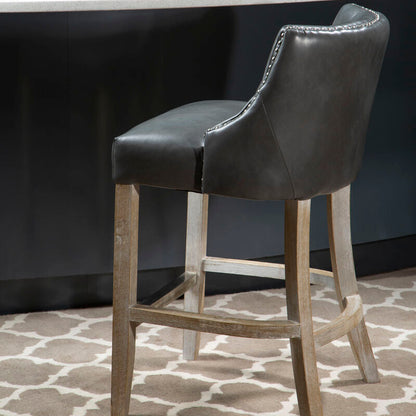 Gray bar stool with wooden legs in front of a white countertop with a plant on it.