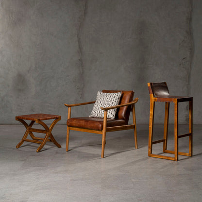 Brown leather chair with patterned pillow and two wooden side tables against a gray wall.
