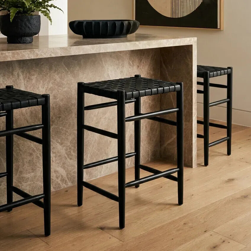 Black bar stools with woven seat design in a room with a counter and decor.