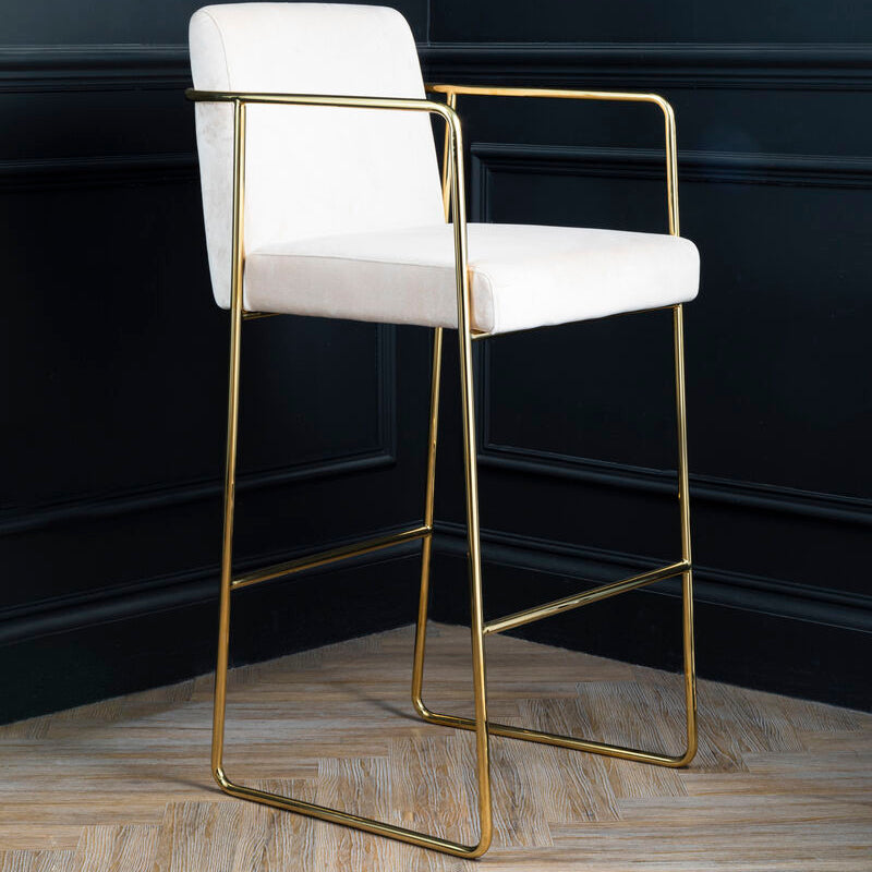 White bar stool with gold frame against a dark paneled wall.