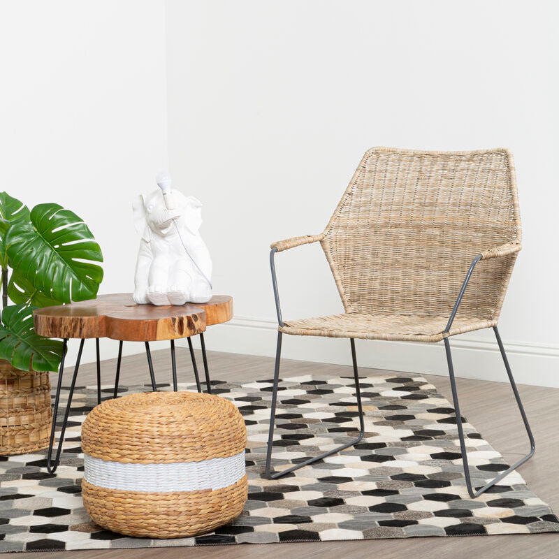 Wicker chair and ottoman on a checkered rug with a plant and small table in the background.