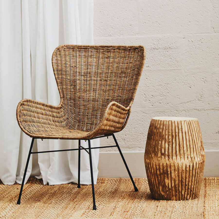 Wicker chair and ottoman against a white curtain and wall.