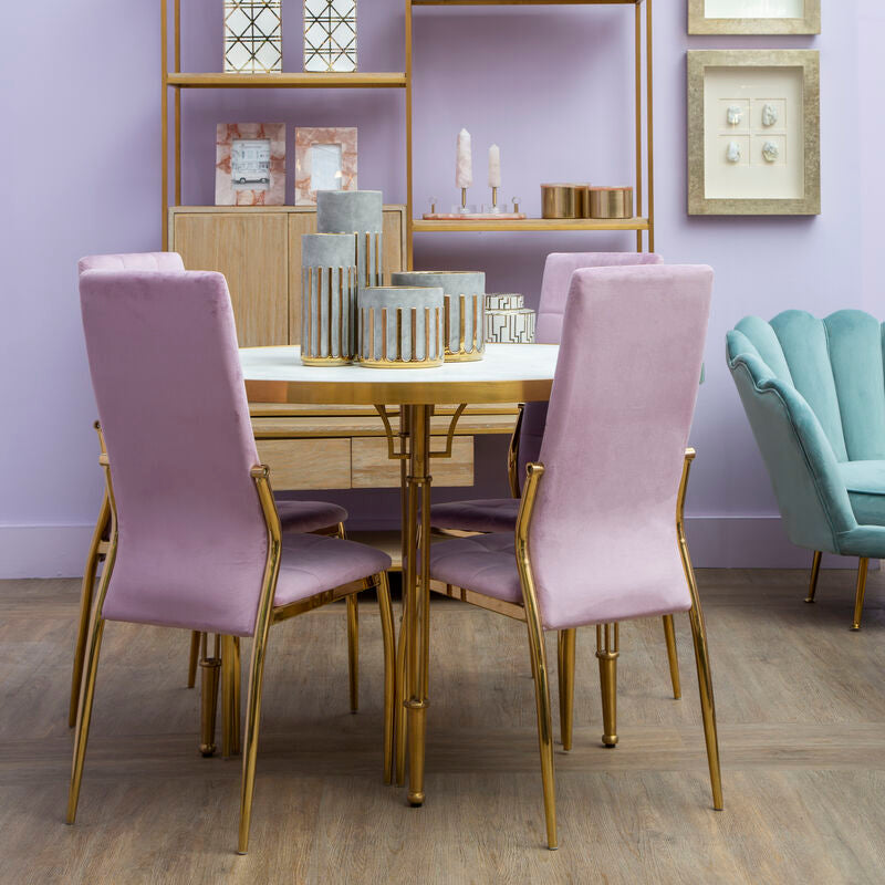 Dining room with pink chairs, gold table, and decorative shelves against a purple wall.