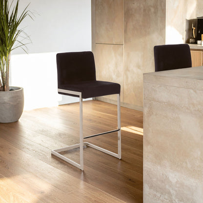 Modern black bar stool with metal legs in a room with wooden floor and light-colored walls.