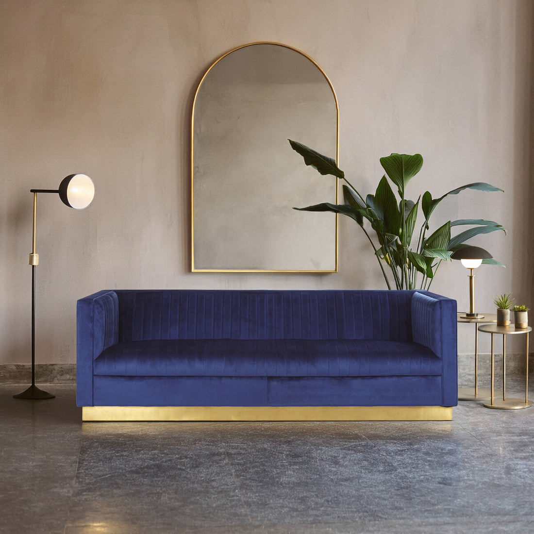 Blue sofa with gold base in a room with a mirror, plant, and floor lamp.