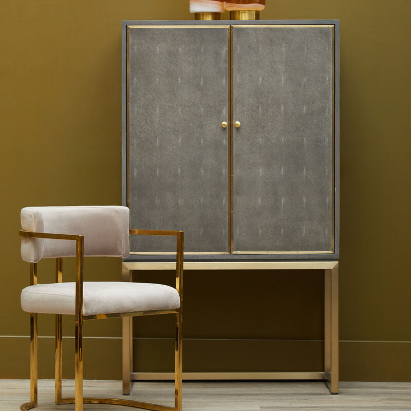 Gray cabinet with gold accents and two stools against a green wall.
