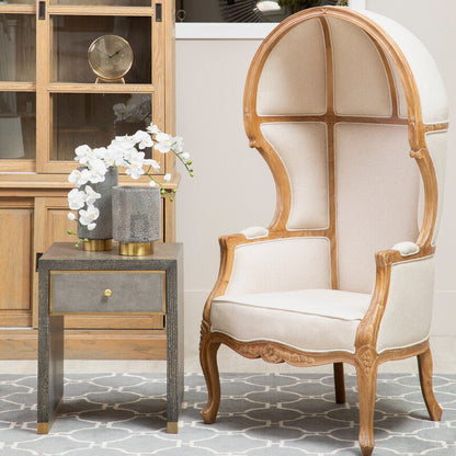 Decorative chair with wooden frame and white cushion in a room with a side table and cabinet.