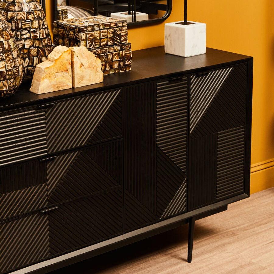 Black geometric-patterned sideboard with decorative items against a yellow 