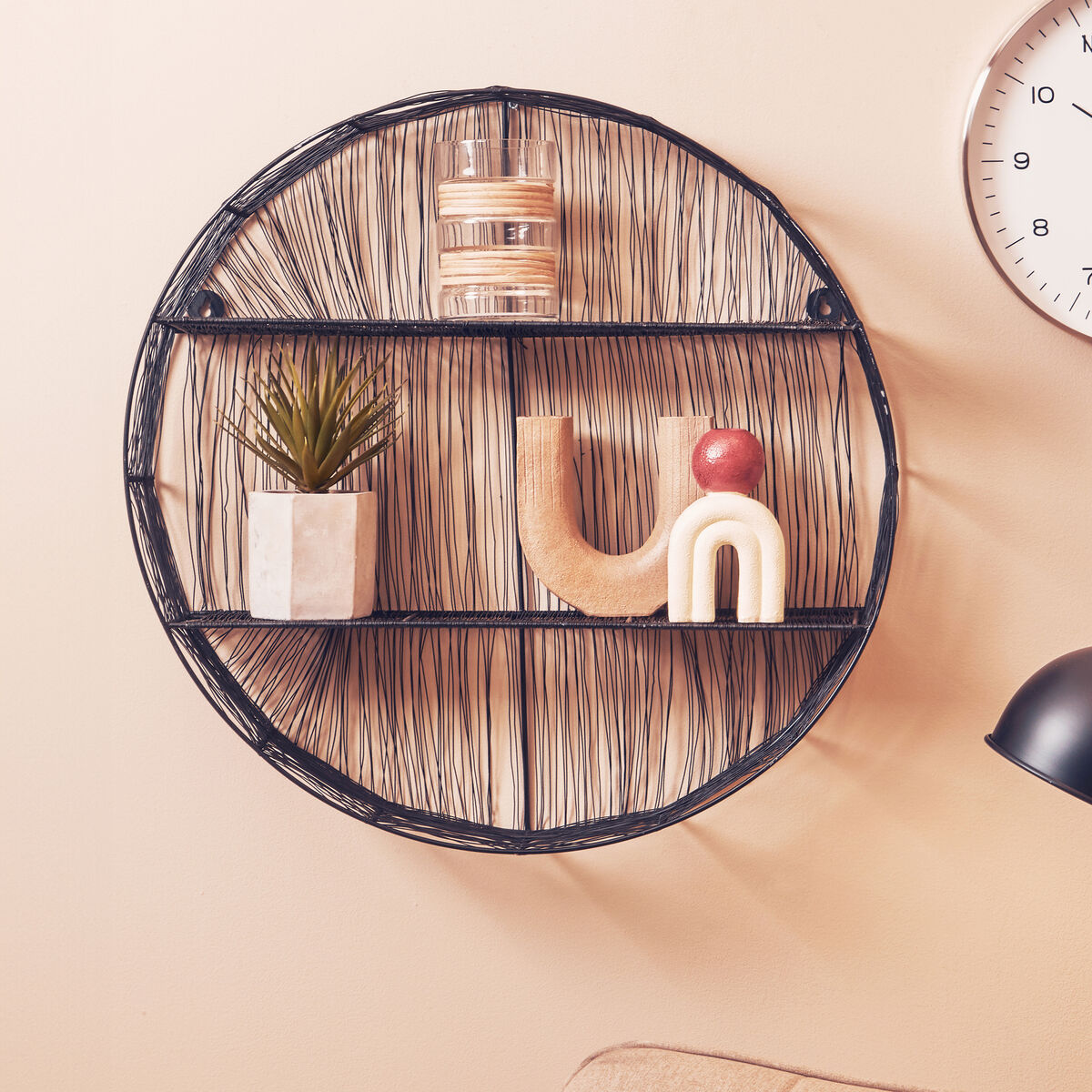 Round woven wall shelf with decorative items on a beige wall.