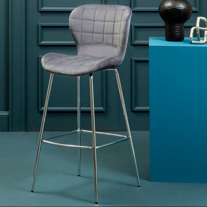 Gray bar stool next to a blue pedestal with decorative items against a teal paneled wall.