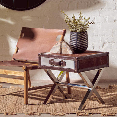 Brown leather chair and side table with a vase of flowers against a white brick wall.