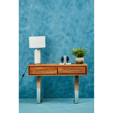 Wooden console table with a lamp and plant against a blue textured wall