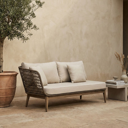 Outdoor sofa with beige cushions next to a potted plant and small table against a beige wall.