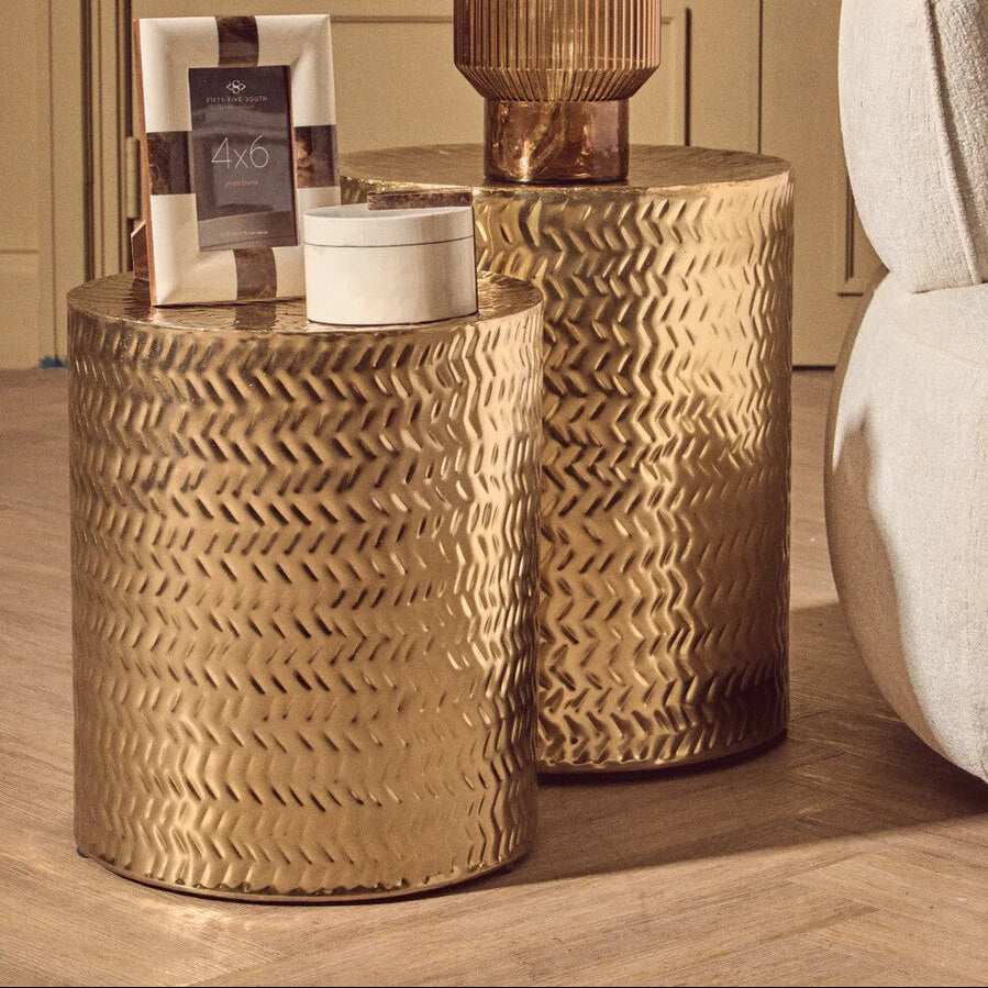 Two gold side tables with decorative items on a wooden floor.