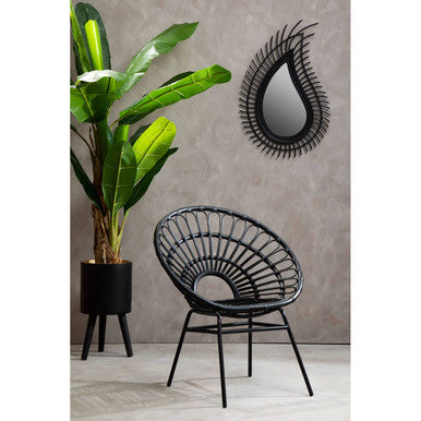 Black wicker chair next to a potted plant and decorative mirror on a gray wall.