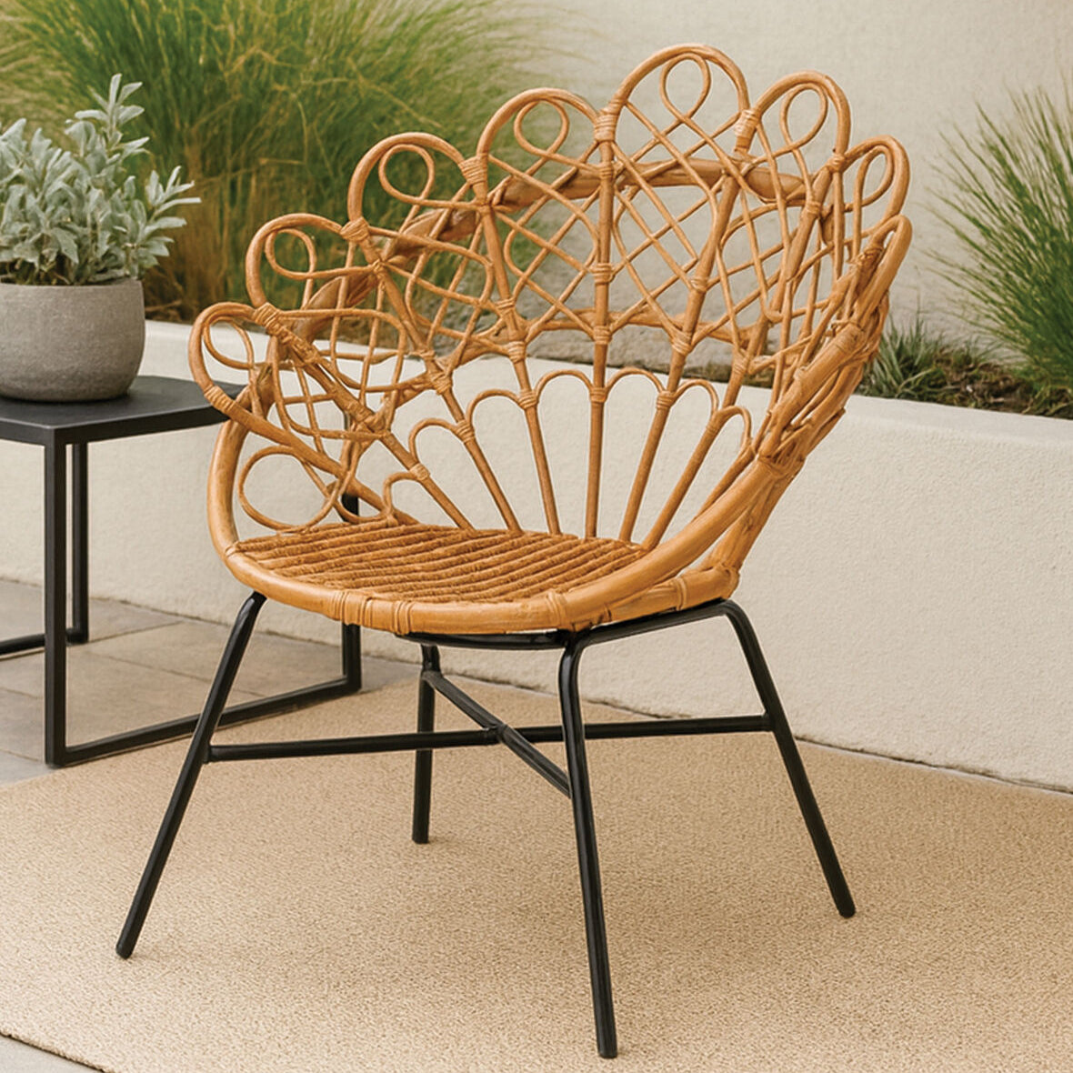Wicker chair with black metal legs on a patio with plants in the background