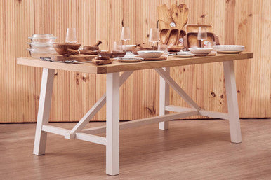 Wooden dining table with white legs against a wooden wall.
