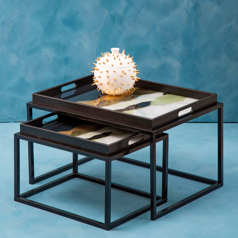 Nest of black metal tables with decorative items against a blue textured wall.
