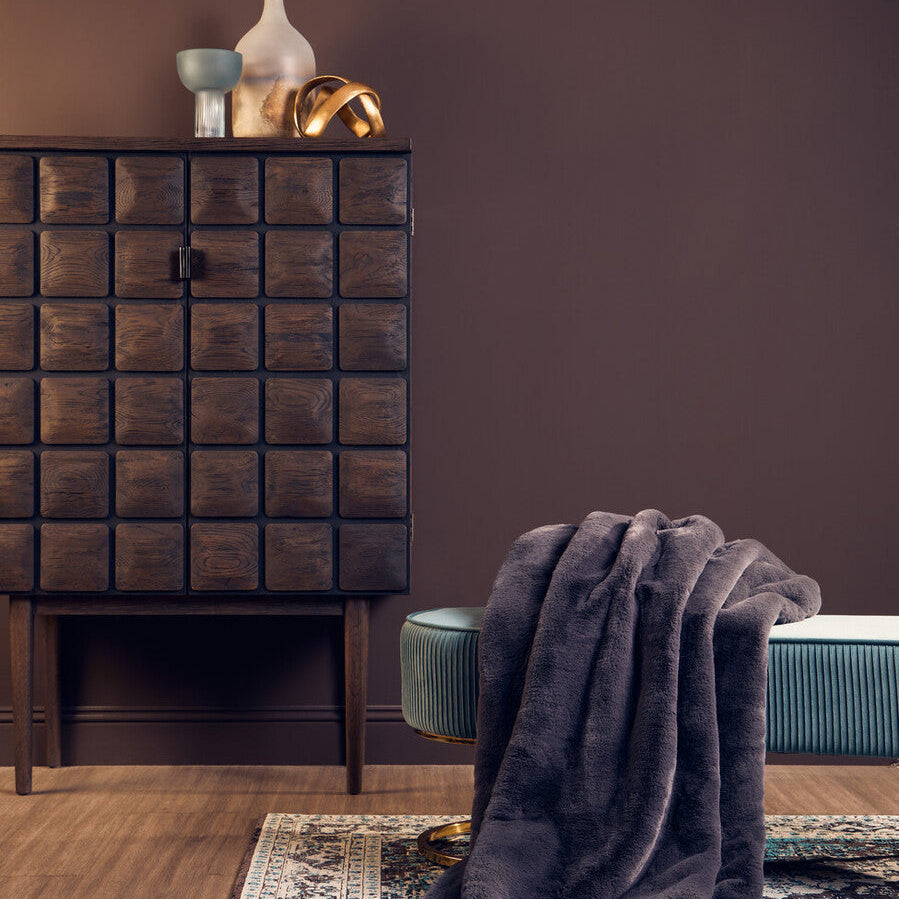 Room interior with a dark brown cabinet, gray blanket, and green chair against a purple wall.