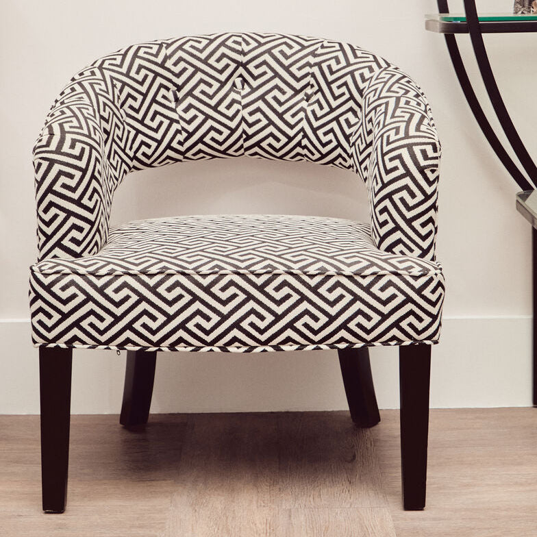 Patterned armchair in a room with a shelf and artwork on the wall.