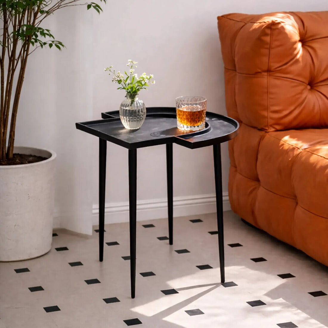 Black side table with a glass of whiskey and a vase of flowers next to an orange sofa.