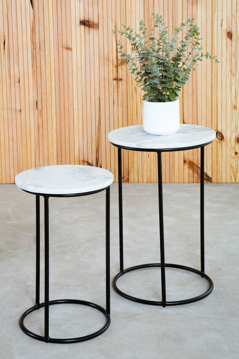 Two marble top side tables with black metal legs against a wooden wall.