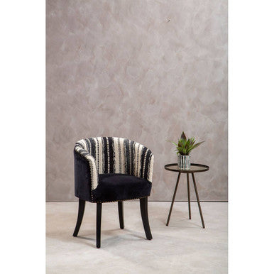 Decorative armchair with striped backrest next to a small round table with a plant against a plain wall.