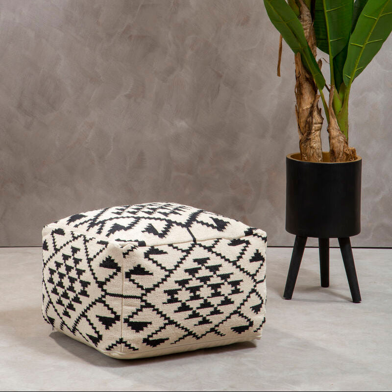 Patterned ottoman next to a potted plant against a gray wall.