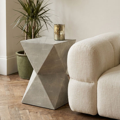 Geometric concrete side table next to a beige sofa and potted plant in a room.