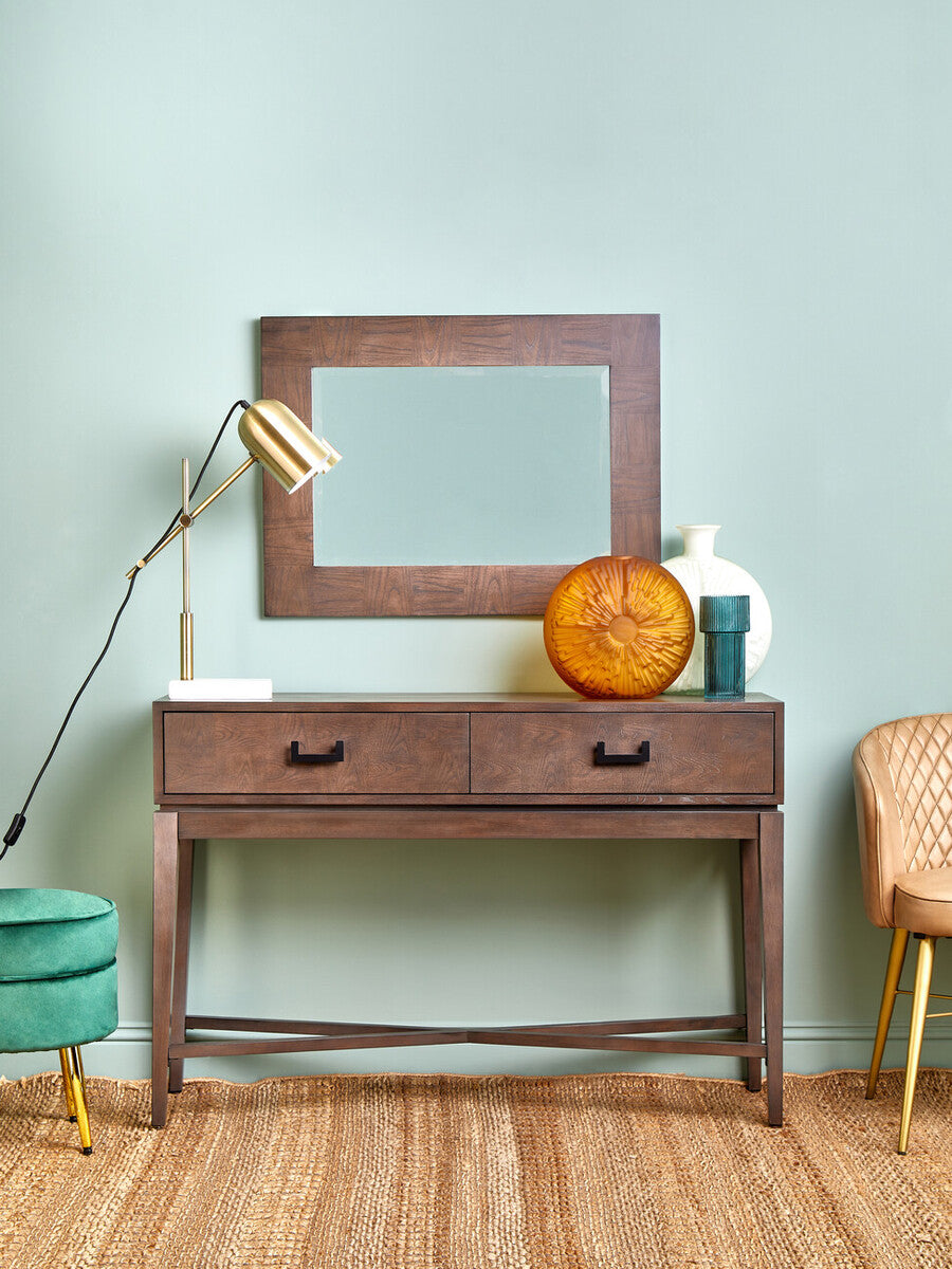 Wooden console table with mirror, lamp, and decorative items against a light green wall.