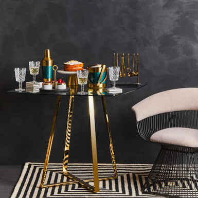 Decorative table with gold and black design against a dark wall with a chair.
