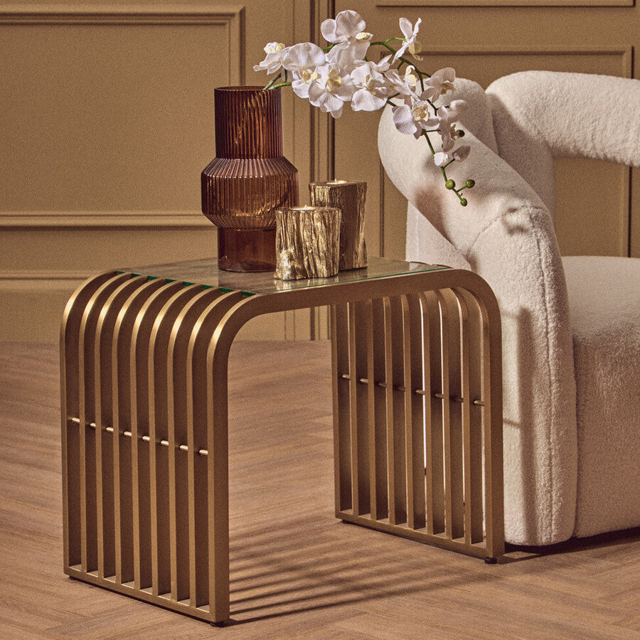 Gold side table with decorative items against a beige wall