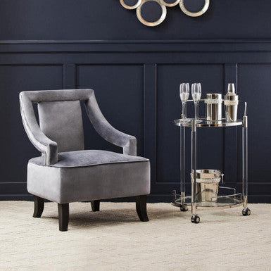 Gray armchair in a room with a decorative wall piece and a glass-topped cart.